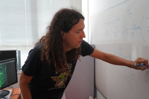 Santiago Oviedo junto a una imagen del experimento que ha validado su investigación teórica, cuya fórmula principal aparece en la pizarra.