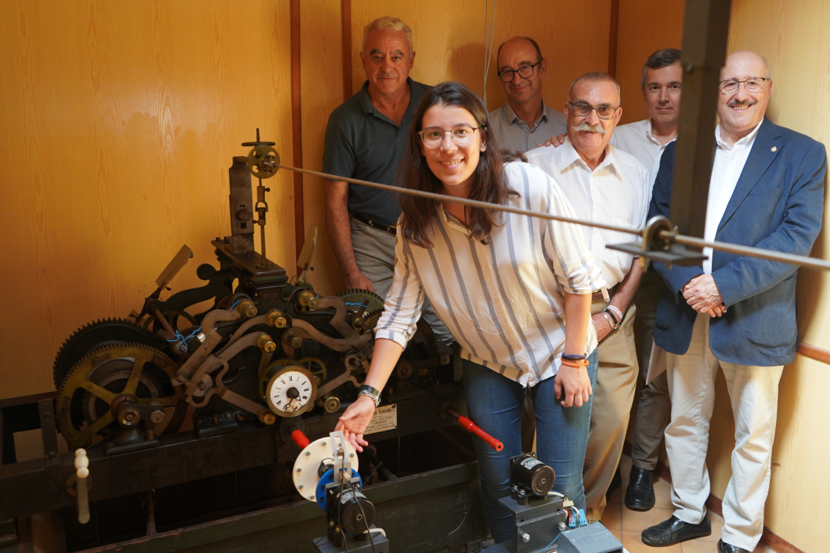 Laura Salas conectando el sistema que ha diseñado al reloj del siglo XIX; detrás, profesores y técnicos de la UPCT junto a responsables de la Sociedad.